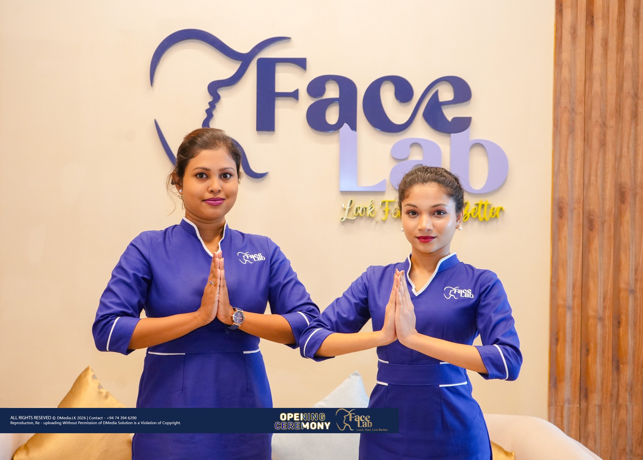 Two FaceLab reception staff greet guests with a namaste in front of the brand wall